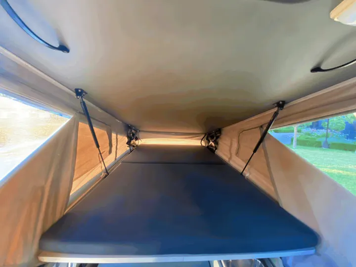 Spacious interior of an RV rental rooftop tent, showcasing a comfortable mattress and lift mechanism, ready for sleep.. Volkswagen T4 Multivan Westfalia 1995