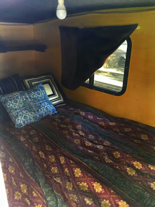 Cozy RV rental camper interior: bed with patterned bedding, pillows, window, shelf. Ideal for travel.. Runaway Campers Navigator 2017