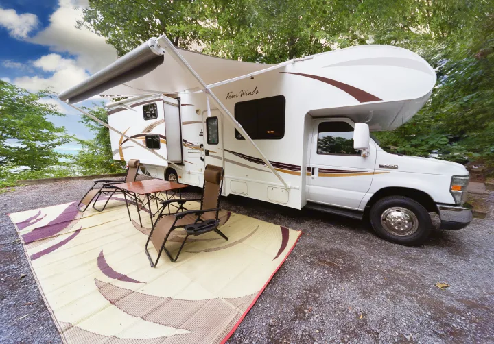 RV rental parked with extended awning, outdoor chairs, and table on a mat, set in a scenic spot near water.. Other Four Winds 2013