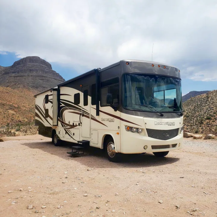 A cream and dark brown Georgetown rv rental, with slide-out extended, is parked in a rugged desert landscape with mountains.. Forest River Georgetown 2015