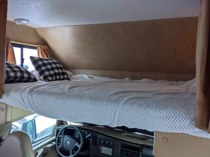 Cozy RV rental sleeping area above the cab, featuring a fluffy bed and plaid pillows. Ideal for your next road trip.. Forest River Forester 2016