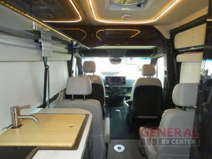 Inside a modern RV rental, showing the front cab, passenger seating, and a compact kitchen area with a sink. Ideal for travel.. Winnebago Era 2021
