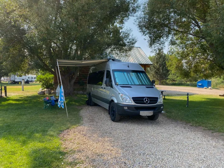 Silver Sprinter rv rental campervan set up for outdoor living at a peaceful campground, awning extended, chairs.. Dodge Sprinter 2500 170ext 2008