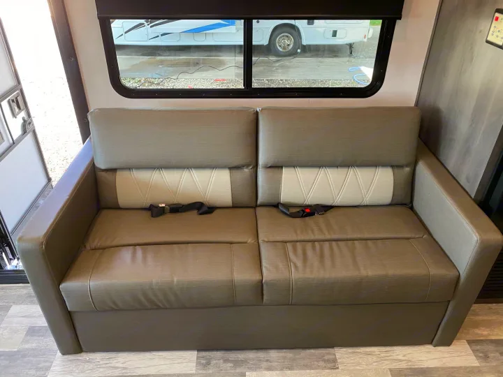 View inside an RV rental: Seating area featuring a gray sofa with safety belts by the window.. Forest River FR3 2021