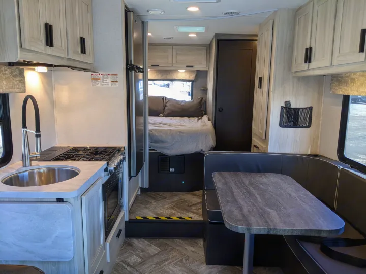 Explore this RV rental's well-designed interior, featuring a full kitchen, comfy bedroom, and spacious dining booth.. Forest River Sunseeker 2025