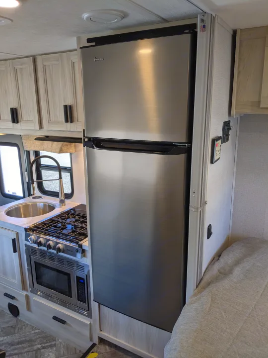 RV rental kitchen features Magic Chef stainless steel fridge, gas cooktop, and microwave. Bright, compact space.. Forest River Sunseeker 2025