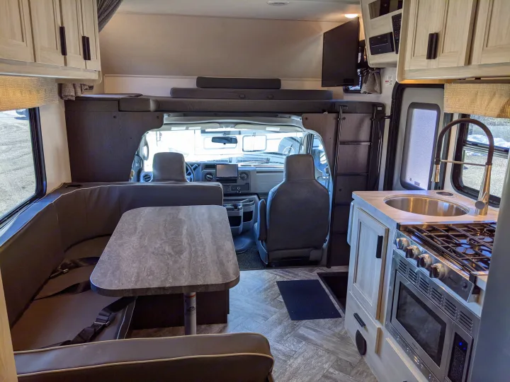 An rv rental interior featuring a dinette with table, kitchen, overhead bunk bed, and front cab.. Forest River Sunseeker 2025