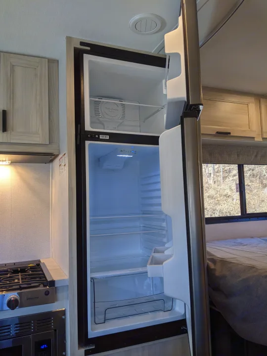 Explore the cozy interior of this RV rental, featuring an open refrigerator, stove, and comfortable bed for travel.. Forest River Sunseeker 2025