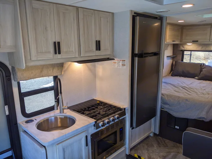 This RV rental interior showcases a compact kitchen with a sink, stove, and fridge, along with a comfortable bedroom area.. Forest River Sunseeker 2025