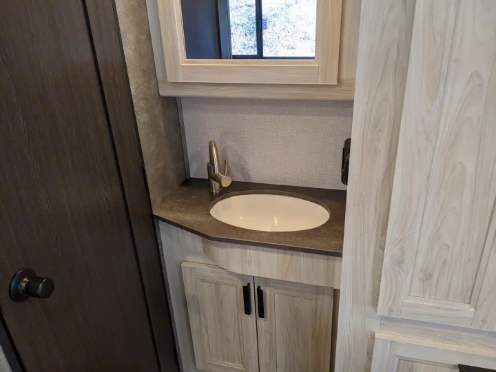 Compact RV rental bathroom with a modern sink, dark countertop, light wood vanity, and mirrored cabinet.. Forest River Sunseeker 2025