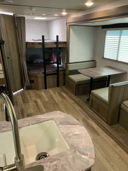This RV rental interior features bunk beds, a dinette booth with a table, and a kitchen area with a sink.. Gulf Stream Kingsport 2021