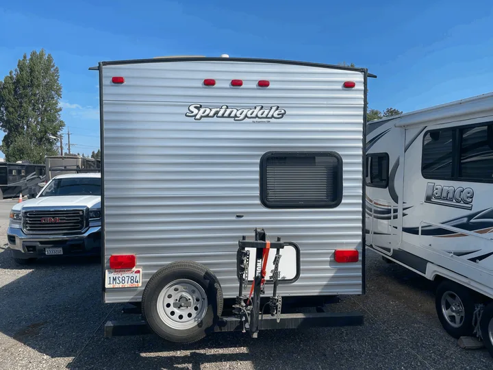 Rear view of a silver Springdale travel trailer, featuring a spare tire and bike rack, perfect for RV rental adventures.. Keystone Springdale 2017