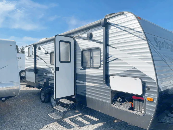 Springdale travel trailer (RV) for rental, parked outdoors. Side view shows open door with steps and accessible storage.. Keystone Springdale 2017