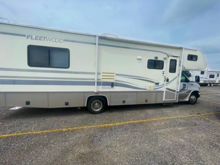 Side view of a large white and grey Fleetwood RV rental parked on an asphalt lot, ready for adventure.. Fleetwood Tioga 2000