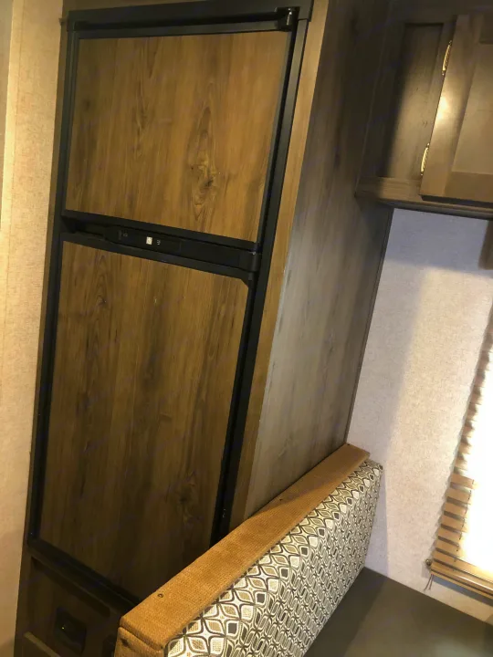 RV rental interior with a wood-paneled refrigerator and a patterned dinette bench.. Coachmen Clipper 2019