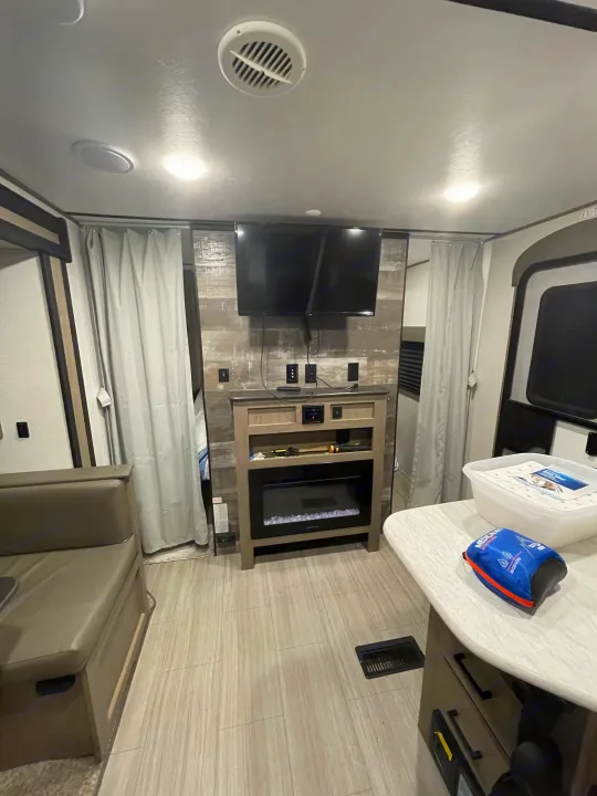 Modern RV rental living area features dual TVs, an electric fireplace, and stylish wood-look flooring. A comfortable space.. Keystone Hideout 2021