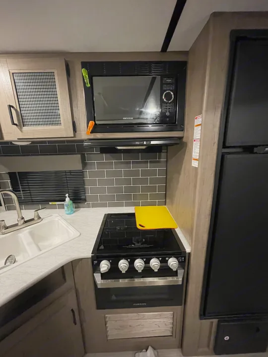 RV rental kitchen: light wood cabinets, double sink, stove, microwave & fridge. Compact, modern setup for travel.. Keystone Hideout 2021