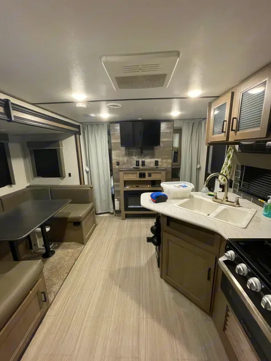 An RV rental's modern interior features a comfortable dinette, functional kitchen with sink and stove, and an entertainment center with TV.. Keystone Hideout 2021