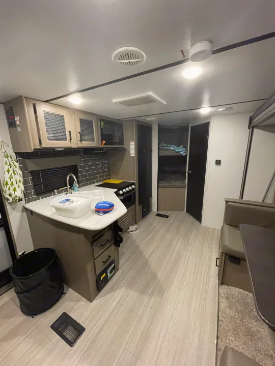 Modern RV rental interior with compact kitchen, dining booth, and bunk bed sleeping area.. Keystone Hideout 2021