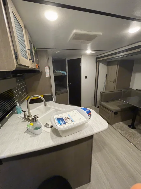 An RV rental features a well-equipped kitchen with a sink, comfortable bunk beds, and a dining booth, ideal for travel.. Keystone Hideout 2021