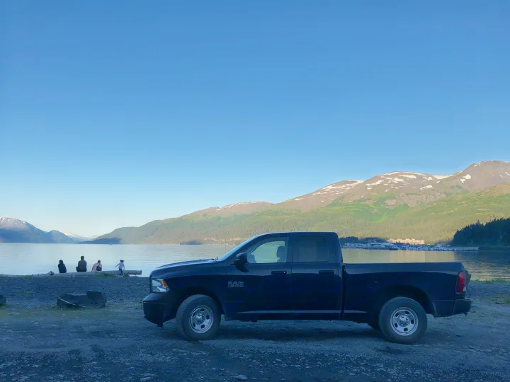Serene mountain lake scene: family by the water, a black pickup truck, perfect stop on an RV rental journey.. Dodge 1500 2013