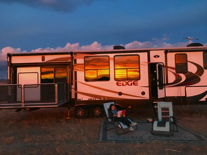 Vibrant sunset on an RV rental. A person relaxes outside by the camper, with stunning reflections in the windows. Living the lifestyle!. Heartland Edge 2016