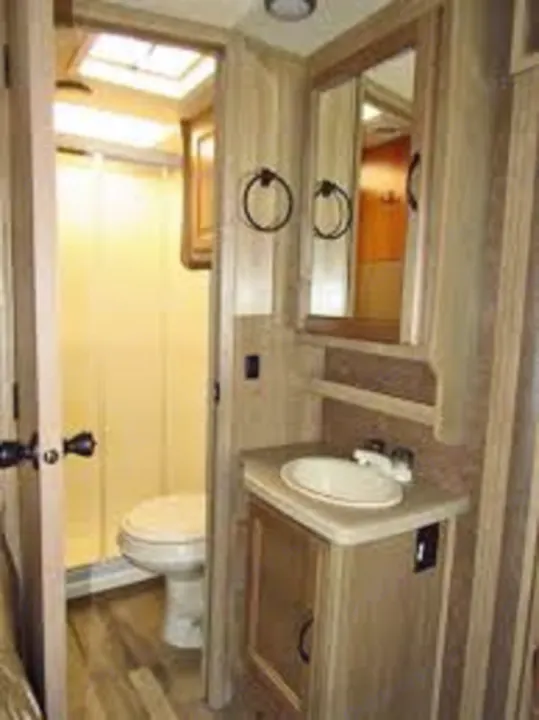 RV rental bathroom features a compact vanity with sink & mirror, next to a shower/toilet area. Light wood interior.. Coachmen Prism 2016
