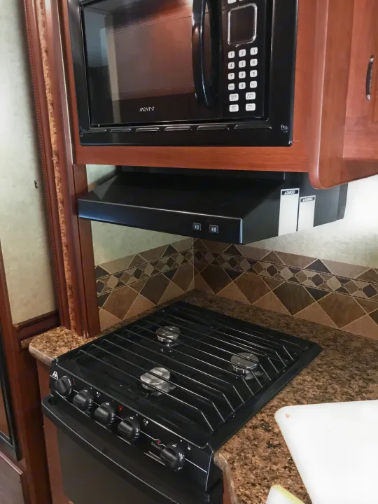RV rental kitchen showcasing a black microwave, range hood, and stove/cooktop with a tiled backsplash and granite countertop.. Thor Motor Coach Freedom Elite 2015