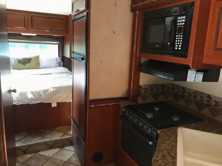 Cozy RV rental interior featuring a kitchen with microwave, stove, fridge, and a comfortable bedroom area.. Thor Motor Coach Freedom Elite 2015