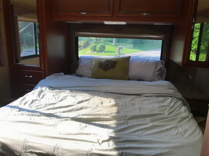 An inviting RV rental bedroom with a comfortable bed, soft pillows, and a window view of the outdoors. Perfect for travel.. Thor Motor Coach Freedom Elite 2015
