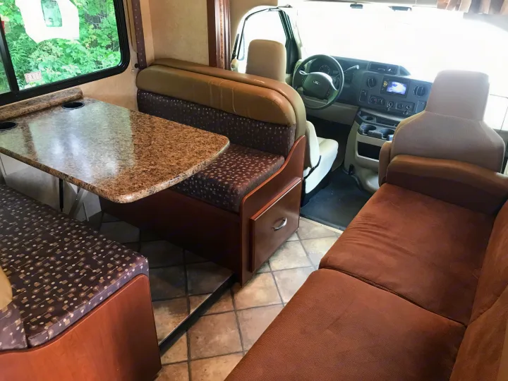 RV rental interior: A bright, cozy space with a dinette, brown sofa, and front cabin with Ford steering wheel visible.. Thor Motor Coach Freedom Elite 2015