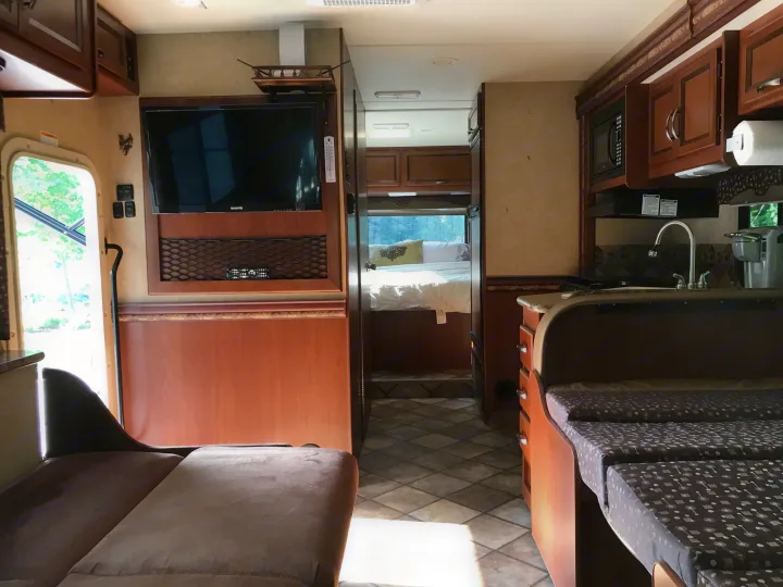 Spacious rv rental interior: living area with TV, kitchen (sink, microwave), and cozy rear bedroom. Ready for travel!. Thor Motor Coach Freedom Elite 2015