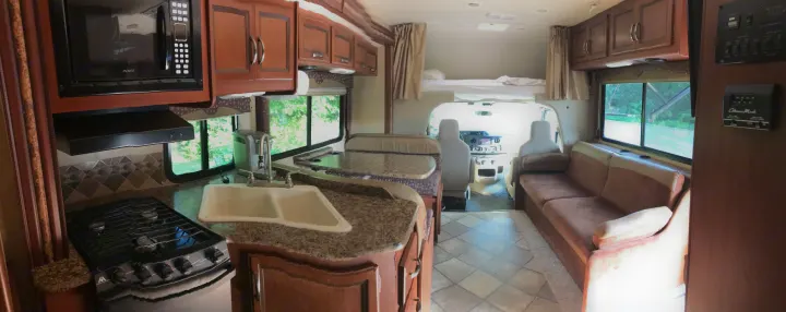 Spacious RV rental interior with a full kitchen, dining booth, comfy sofa, driver's cab, and an overhead bunk bed.. Thor Motor Coach Freedom Elite 2015