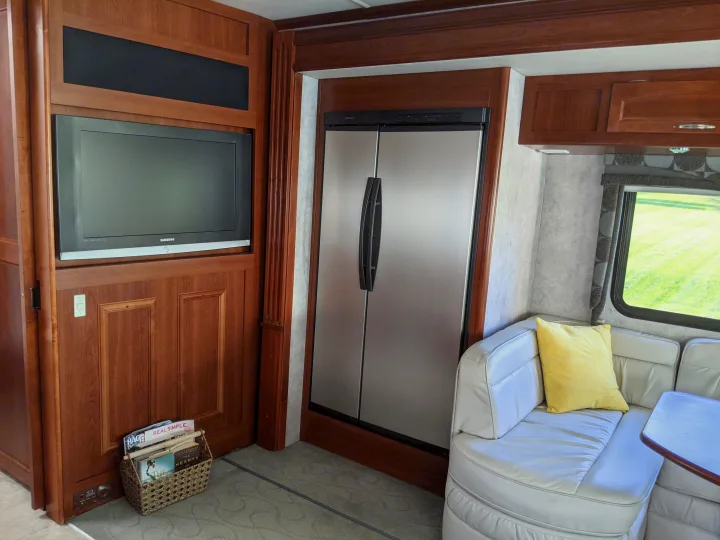 Cozy RV rental living space featuring a flat-screen TV, stainless fridge, and plush corner seating with a yellow pillow.. Fleetwood Pace Arrow 2007