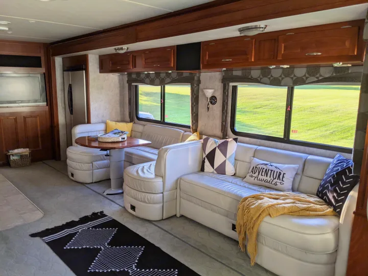 Cozy RV rental interior with comfortable seating, dinette, and bright windows offering a view of green landscape.. Fleetwood Pace Arrow 2007