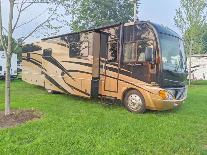 A large black and gold RV rental, a Class A motorhome, is parked on a green campsite ready for travel.. Fleetwood Pace Arrow 2007