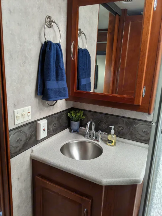 Compact RV rental bathroom vanity with sink, mirror, towel, and light switches, designed for efficient travel.. Fleetwood Pace Arrow 2007