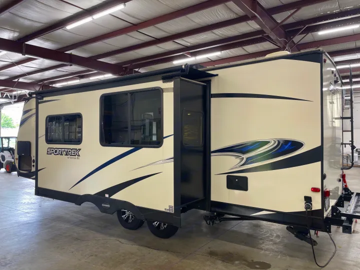 Sporttrek travel trailer RV rental, cream with blue/black graphics and extended slide-out, parked in an indoor garage.. Venture Sport Trek 2017