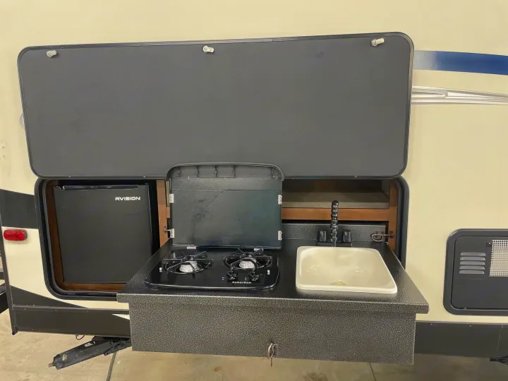 RV rental outdoor kitchen setup with a sink, 2-burner Suburban stove, and RVISION refrigerator for easy outdoor cooking.. Venture Sport Trek 2017