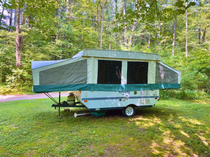 This Rockwood pop-up camper is set up in a lush green forest, ready for an RV rental outdoor adventure.. Forest River Rockwood Freedom 2001