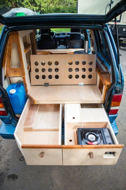 Custom RV rental setup: wooden bed, pull-out kitchen stove & storage in a camper van conversion.. Toyota Hiace 1985