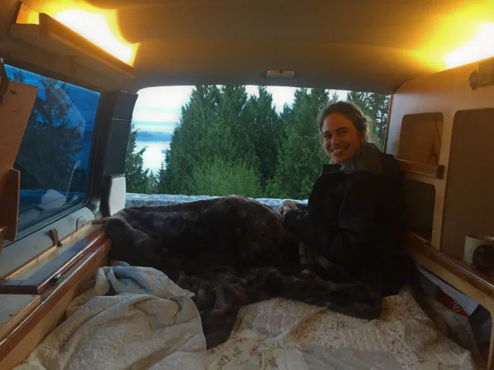 A woman smiles from a cozy rv rental, enjoying the scenic lake and forest view from her comfy camper bed.. Toyota Hiace 1985