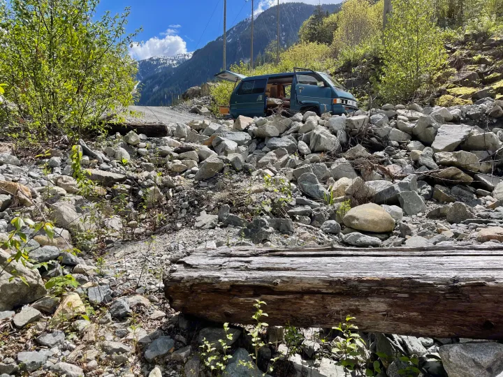 Teal camper van, ideal for RV rental, parked on a rocky mountain road with snowy peaks under a blue sky.. Toyota Hiace 1985