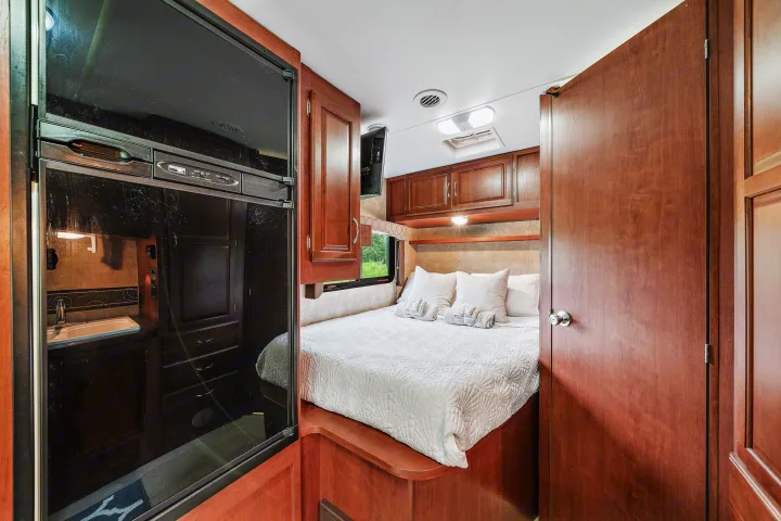A comfy bedroom inside an RV rental, featuring a white bed, wooden cabinets, and a tall black refrigerator on the left.. Winnebago Spirit 2015