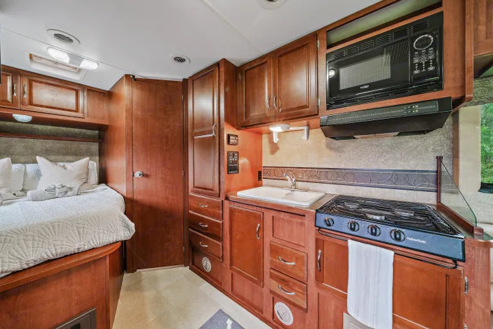 Cozy RV rental interior featuring a compact kitchen with sink, stovetop, microwave, and a comfortable bed area.. Winnebago Spirit 2015
