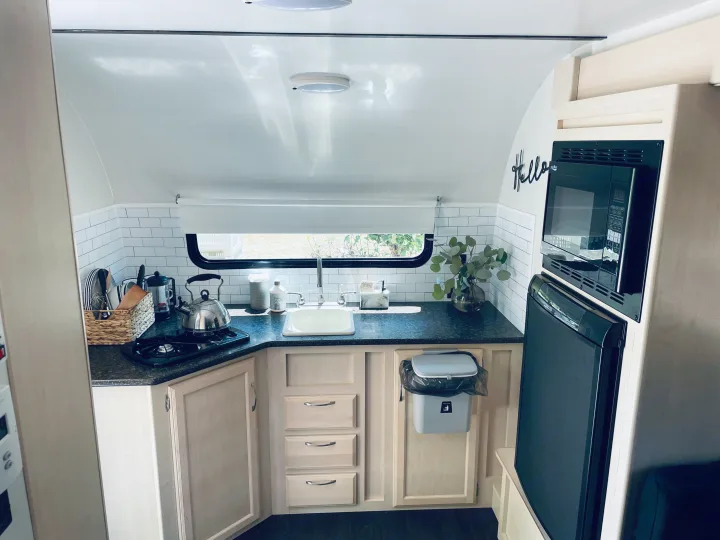 This modern RV rental kitchen features a compact stove, sink, microwave, fridge, and neat subway tile backsplash.. Winnebago Minnie Winnie 2018