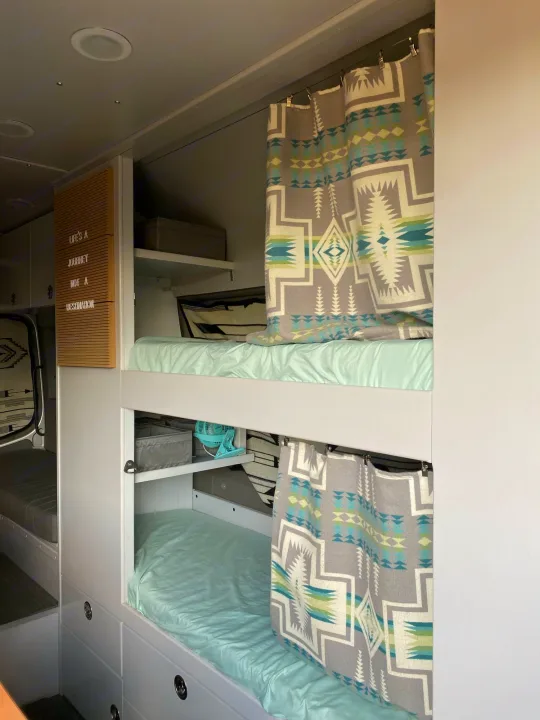 Inside a modern RV rental: light blue bunk beds with geometric patterned curtains, storage, and "Life's a Journey" sign.. Dodge Sprinter 2500 170ext 2008