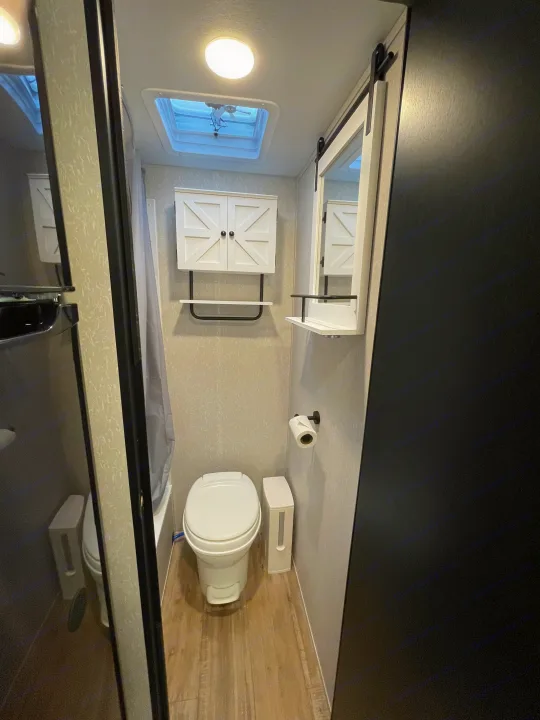 Bright RV rental bathroom with a toilet, shower, wall cabinet, mirror, and skylight. Compact and ready for use.. Forest River Cherokee Wolf Pup 2022