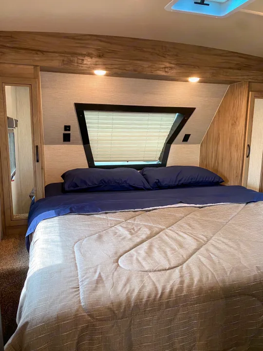 Serene RV rental bedroom featuring a blue-sheeted bed, window blinds, and built-in cabinetry.. Palomino Solaire Ultra Lite 2021