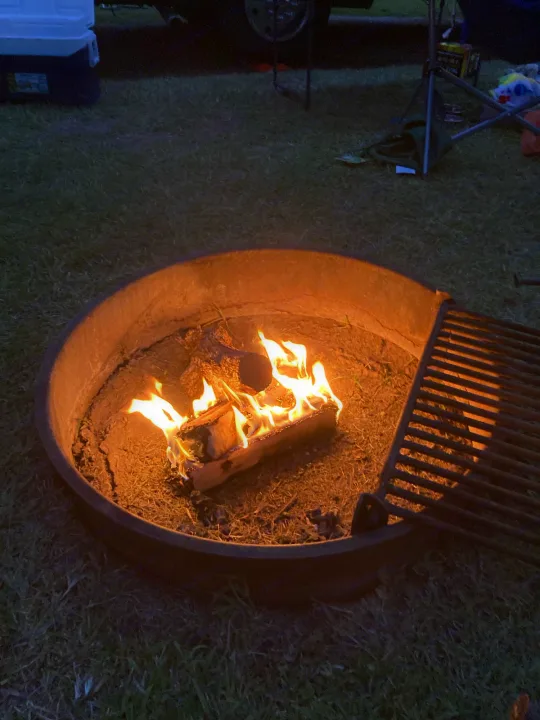 A crackling campfire in a ring with a grill, set in grass. A perfect end to a day on an RV rental trip.. Winnebago Outlook 2020